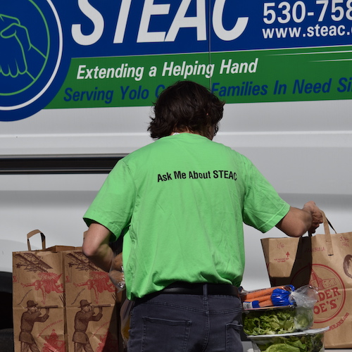 STEAC volunteer holding grocery bags of food in front of a STEAC van
