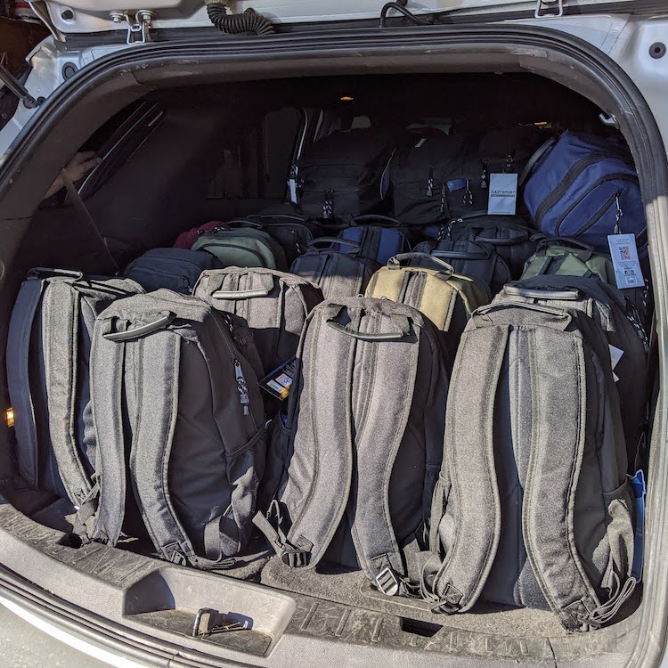 large number of backpacks loaded in back of car