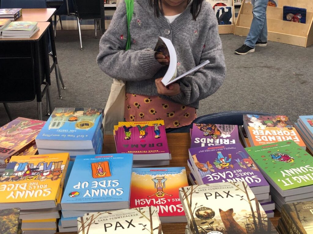 Person reading book from a stack of books on the table