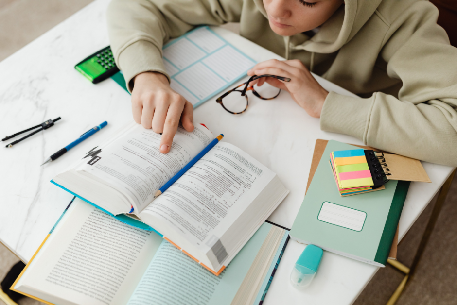 Photo of student holding glasses and pointing at a textbook.